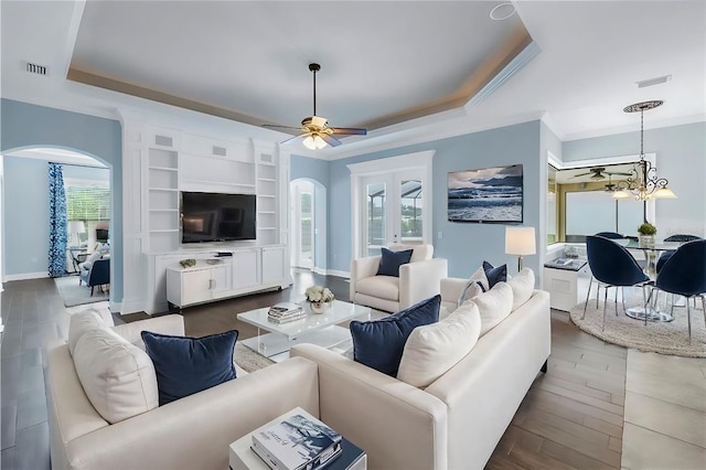 living room with a raised ceiling, ceiling fan, built in features, hardwood / wood-style flooring, and ornamental molding