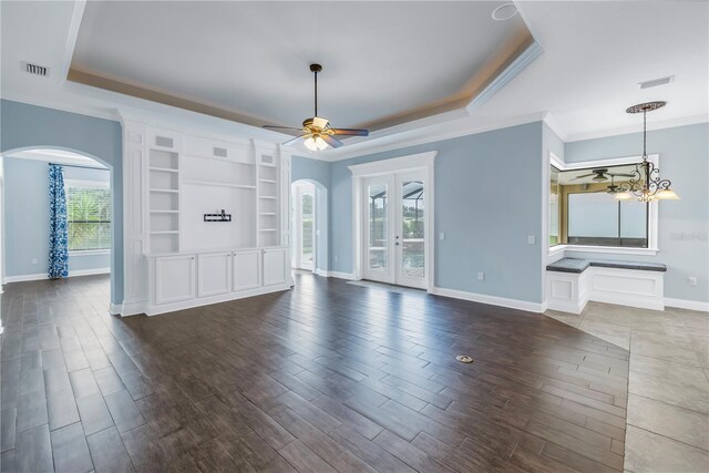 unfurnished living room with ceiling fan with notable chandelier, a tray ceiling, and a wealth of natural light