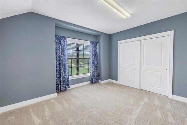 unfurnished bedroom featuring light carpet, a closet, and vaulted ceiling