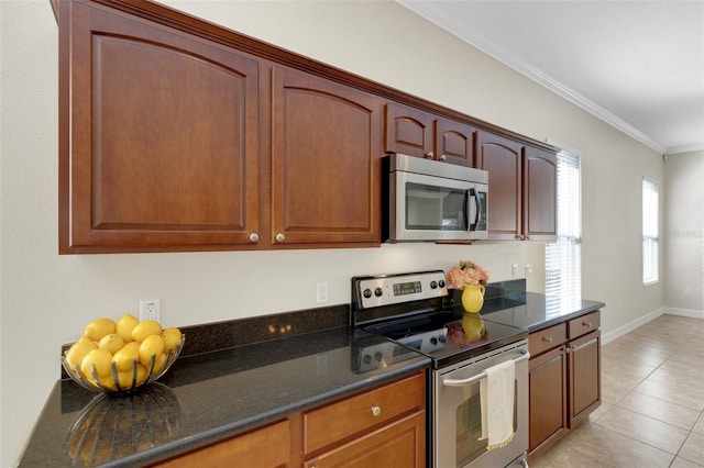 kitchen with appliances with stainless steel finishes, crown molding, dark stone countertops, and light tile patterned floors