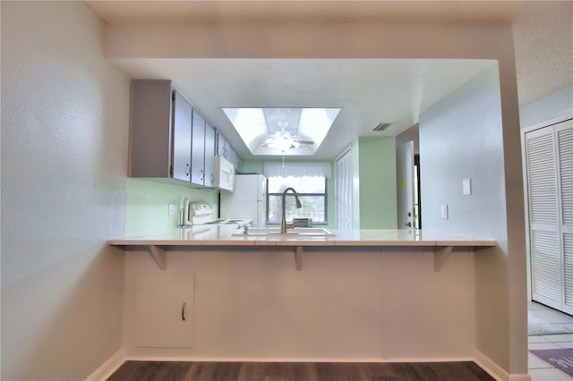 kitchen with white appliances, kitchen peninsula, wood-type flooring, a skylight, and sink