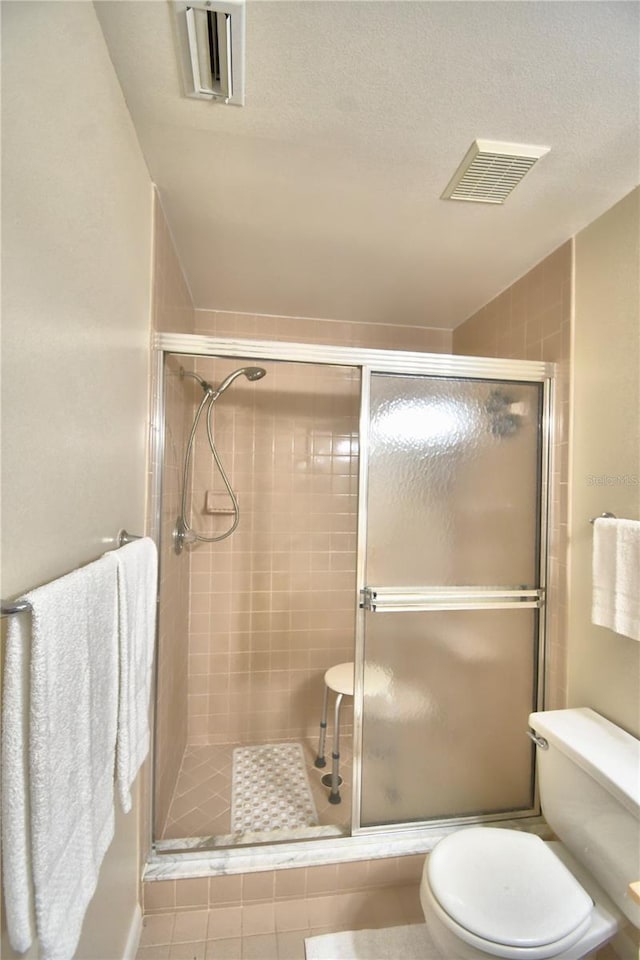 bathroom with tile patterned flooring, a textured ceiling, an enclosed shower, and toilet