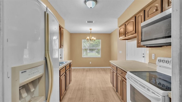 kitchen featuring white appliances, hanging light fixtures, light hardwood / wood-style floors, and a chandelier