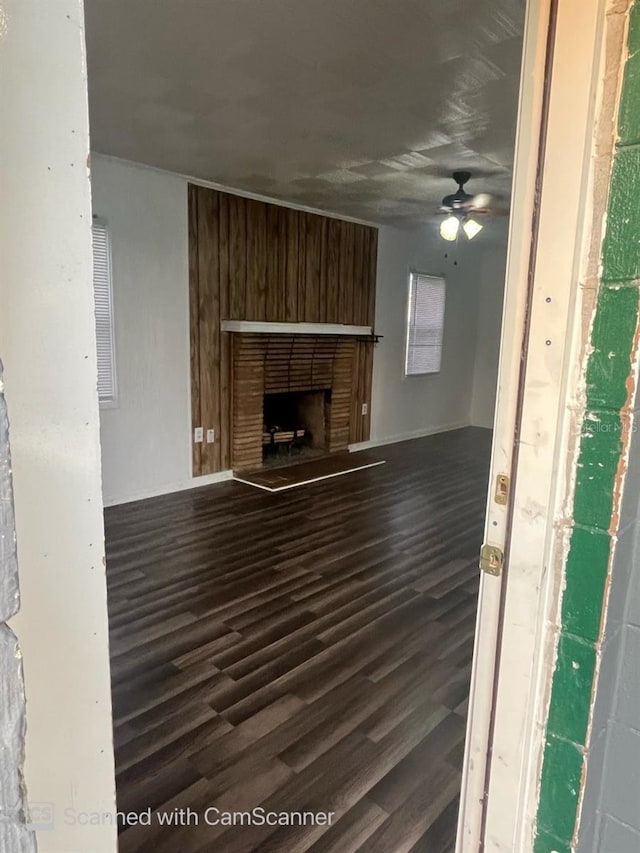 unfurnished living room with wood walls, ceiling fan, dark hardwood / wood-style floors, and a brick fireplace