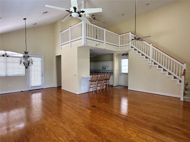 unfurnished living room featuring hardwood / wood-style flooring, ceiling fan with notable chandelier, and high vaulted ceiling