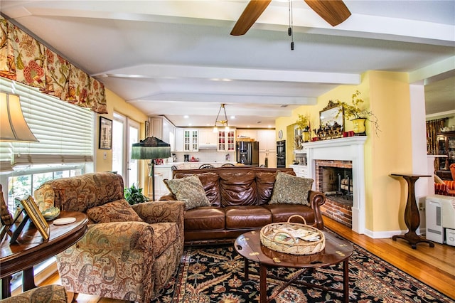 living room featuring a brick fireplace, ceiling fan, beamed ceiling, and hardwood / wood-style flooring