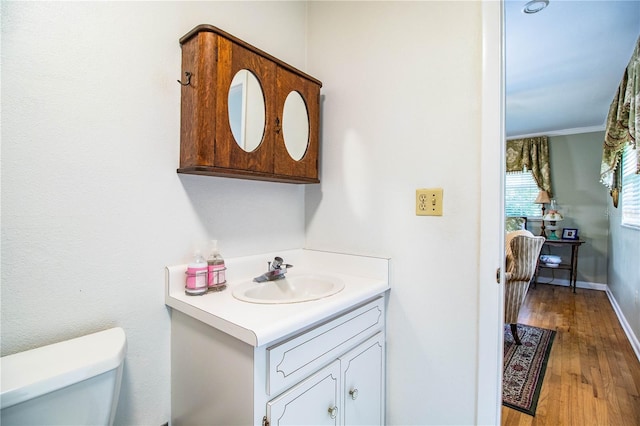 bathroom with hardwood / wood-style flooring, vanity, toilet, and ornamental molding