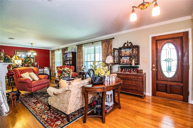 living room with light wood-type flooring, ornamental molding, a textured ceiling, and a chandelier