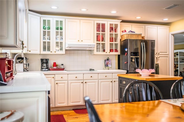 kitchen with backsplash, white cabinets, black electric stovetop, sink, and stainless steel fridge