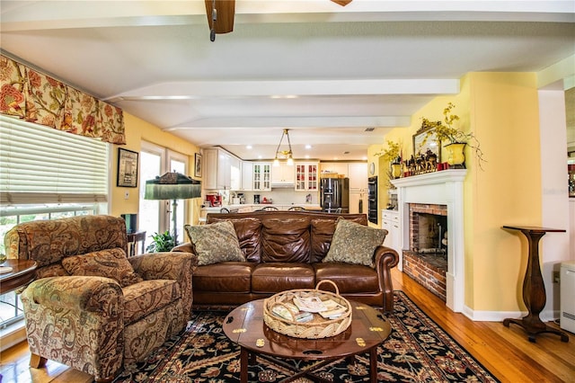 living room featuring beamed ceiling, a healthy amount of sunlight, hardwood / wood-style floors, and a brick fireplace