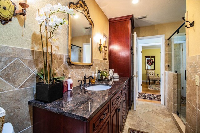 bathroom featuring decorative backsplash, tile patterned floors, an enclosed shower, vanity, and tile walls