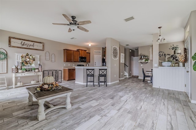 living room with ceiling fan with notable chandelier and light hardwood / wood-style floors