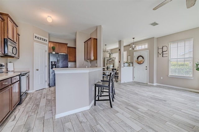 kitchen with light wood-type flooring, electric range, a kitchen breakfast bar, decorative light fixtures, and black refrigerator with ice dispenser