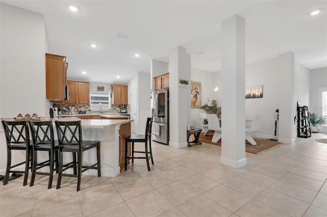 kitchen with light stone counters, light tile patterned floors, kitchen peninsula, backsplash, and appliances with stainless steel finishes