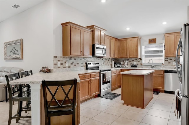 kitchen featuring appliances with stainless steel finishes, kitchen peninsula, a kitchen island, a kitchen bar, and sink