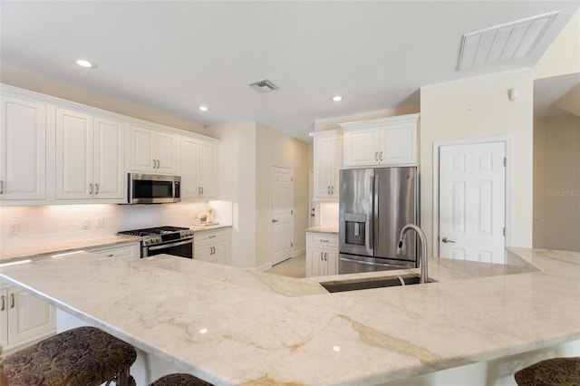 kitchen featuring a breakfast bar, sink, stainless steel appliances, decorative backsplash, and white cabinets