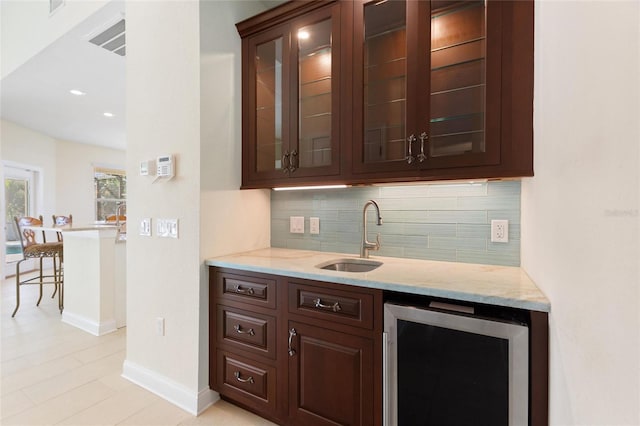 bar featuring sink, dark brown cabinets, beverage cooler, light stone countertops, and decorative backsplash