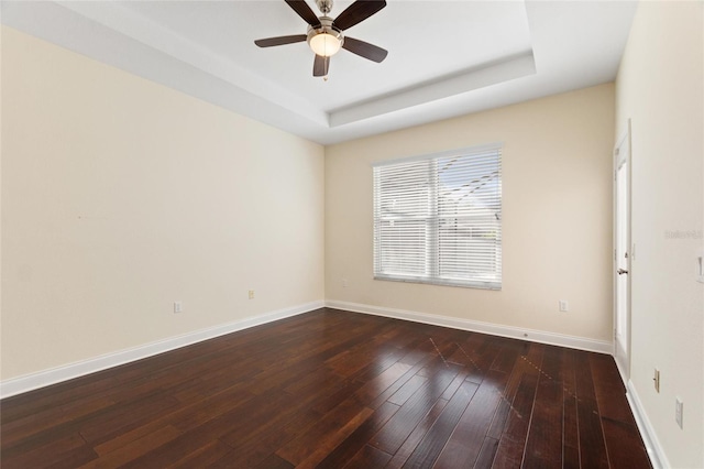 empty room featuring dark hardwood / wood-style flooring, a raised ceiling, and ceiling fan