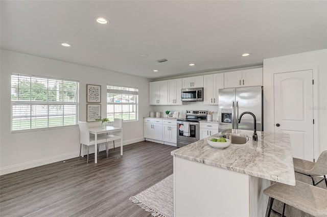4618 Crestview Ln, Lakeland, FL 33813 - kitchen with stainless steel appliances, white cabinetry, a kitchen bar, dark wood-type flooring, and light stone counters