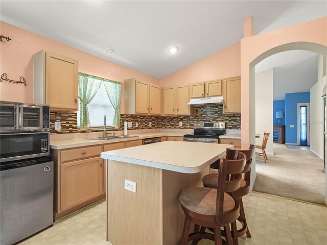 kitchen featuring lofted ceiling, a kitchen island, light brown cabinetry, and stainless steel appliances