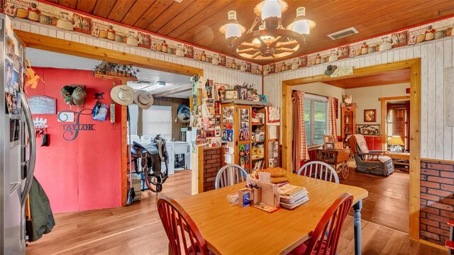 dining space with wooden ceiling, wood walls, light hardwood / wood-style flooring, and a notable chandelier