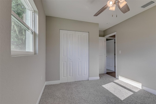 unfurnished bedroom with a closet, carpet, multiple windows, and ceiling fan