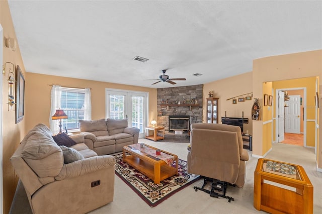 carpeted living room featuring ceiling fan, a stone fireplace, and a textured ceiling