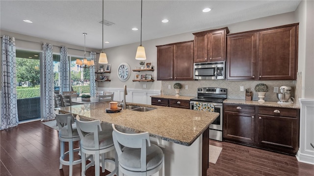 kitchen with light stone counters, sink, an island with sink, hanging light fixtures, and appliances with stainless steel finishes