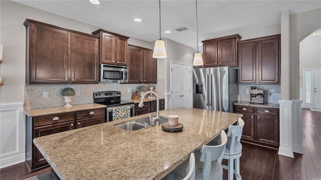 kitchen featuring pendant lighting, dark hardwood / wood-style floors, sink, a center island with sink, and appliances with stainless steel finishes