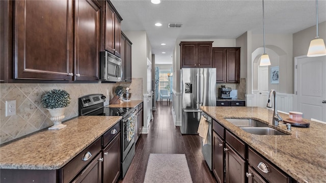 kitchen featuring pendant lighting, dark wood-type flooring, sink, stainless steel appliances, and light stone countertops