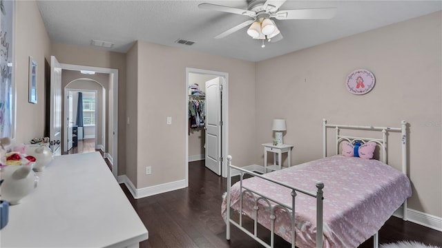 bedroom featuring a spacious closet, dark wood-type flooring, a closet, a textured ceiling, and ceiling fan