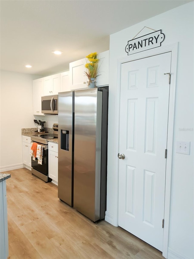 kitchen with white cabinets, appliances with stainless steel finishes, light stone countertops, and light hardwood / wood-style flooring