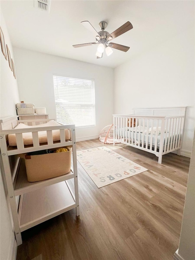 bedroom with ceiling fan, hardwood / wood-style flooring, and a crib