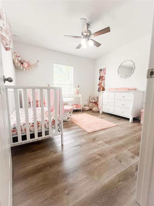 unfurnished bedroom featuring ceiling fan, a nursery area, and hardwood / wood-style floors