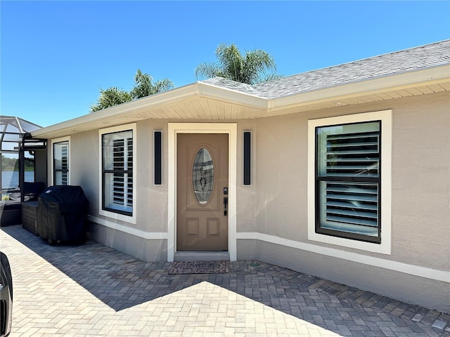 entrance to property featuring stucco siding and a shingled roof