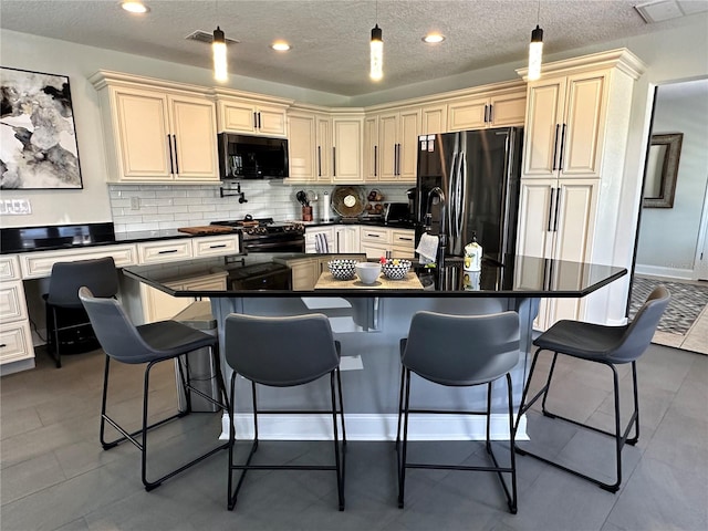 kitchen featuring pendant lighting, a textured ceiling, a kitchen island with sink, black appliances, and a kitchen bar