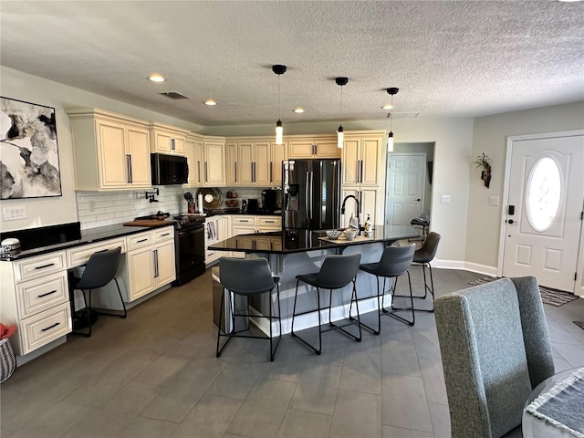 kitchen with a kitchen breakfast bar, a center island with sink, dark countertops, visible vents, and black appliances