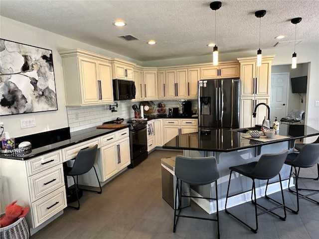 kitchen featuring a sink, tasteful backsplash, dark countertops, black appliances, and cream cabinetry