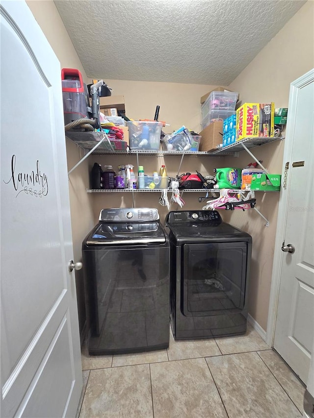 laundry area with washing machine and clothes dryer, a textured ceiling, and light tile patterned floors