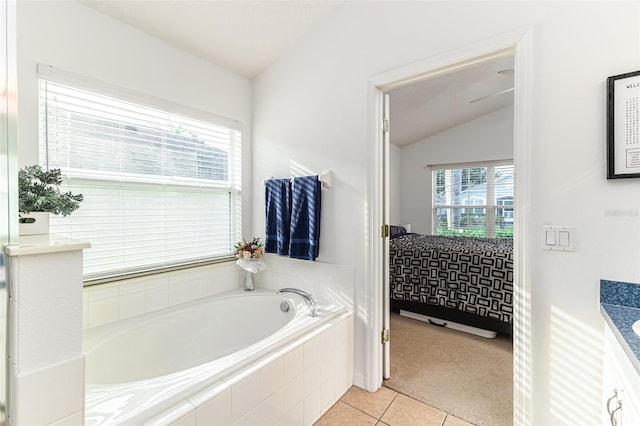 bathroom with tiled tub, vanity, lofted ceiling, and plenty of natural light