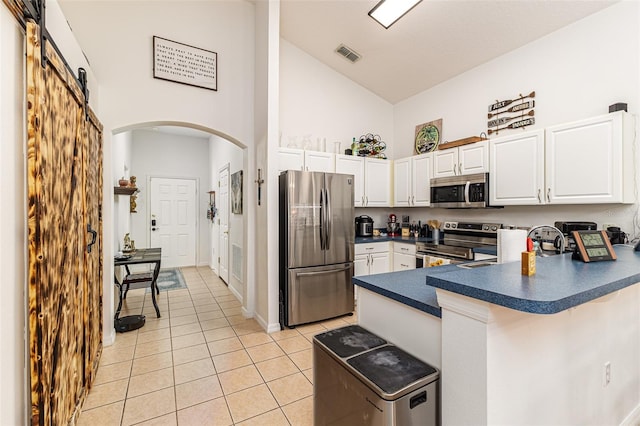 kitchen featuring light tile patterned flooring, white cabinetry, a barn door, high vaulted ceiling, and appliances with stainless steel finishes