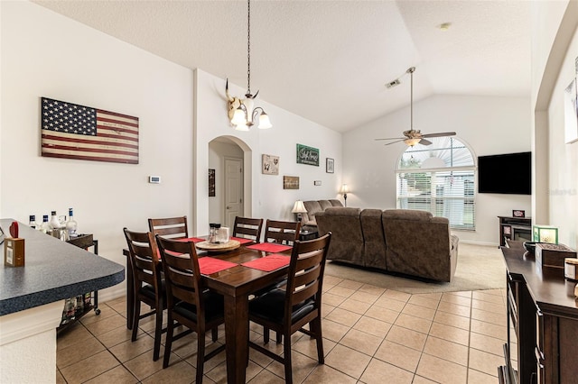 tiled dining space featuring ceiling fan with notable chandelier and vaulted ceiling