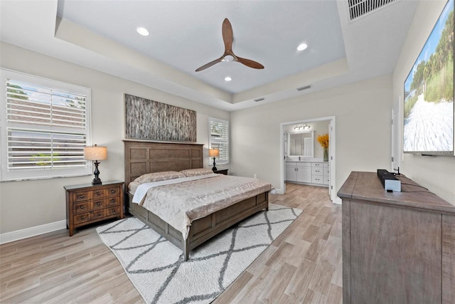 bedroom featuring ceiling fan, light hardwood / wood-style flooring, a raised ceiling, and ensuite bathroom