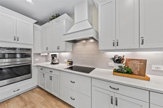 kitchen with light stone counters, black electric cooktop, custom exhaust hood, and white cabinetry