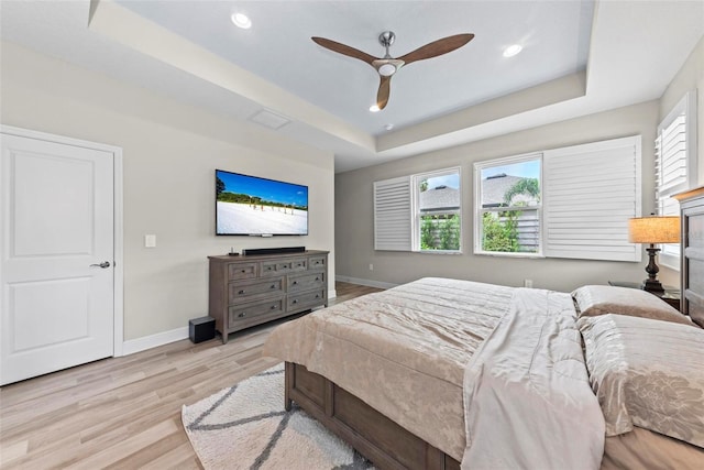 bedroom with light wood-type flooring, ceiling fan, and a raised ceiling