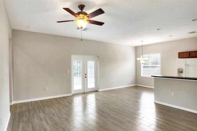 unfurnished living room featuring ceiling fan with notable chandelier and hardwood / wood-style flooring