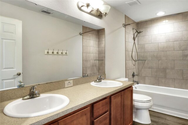 full bathroom with hardwood / wood-style flooring, tiled shower / bath combo, vanity, and toilet