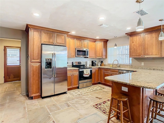 kitchen featuring light stone counters, a breakfast bar, stainless steel appliances, sink, and decorative light fixtures