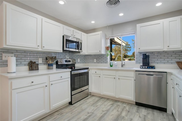 kitchen featuring backsplash, white cabinets, sink, light hardwood / wood-style flooring, and appliances with stainless steel finishes