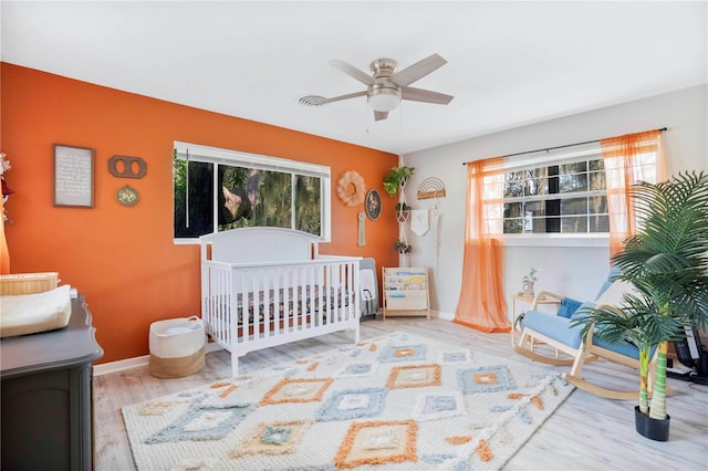 bedroom with ceiling fan, light hardwood / wood-style floors, and a crib